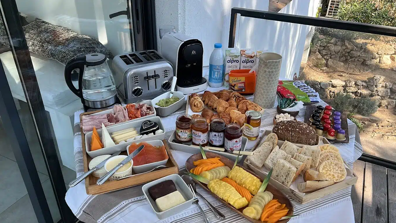 Buffet petit-déjeuner continental extérieur avec charcuterie, fromages, saumon fumé, viennoiseries, fruits frais, pain, confitures et machine à café Philips.