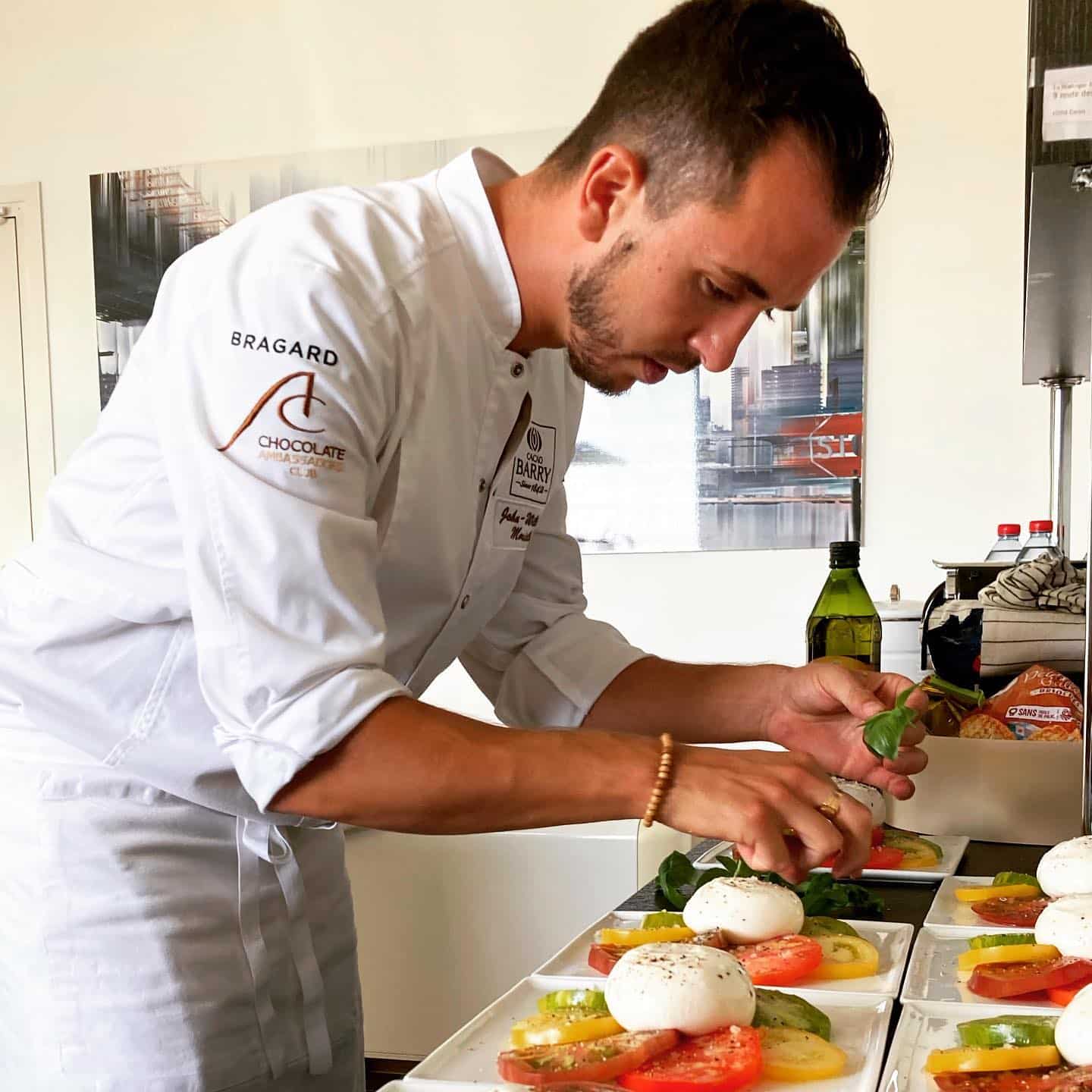 Chef en toque blanche, arborant les logos BRAGARD et CACAO BARRY, prépare méticuleusement des salades Caprese multicolores avec mozzarella, tomates et basilic.