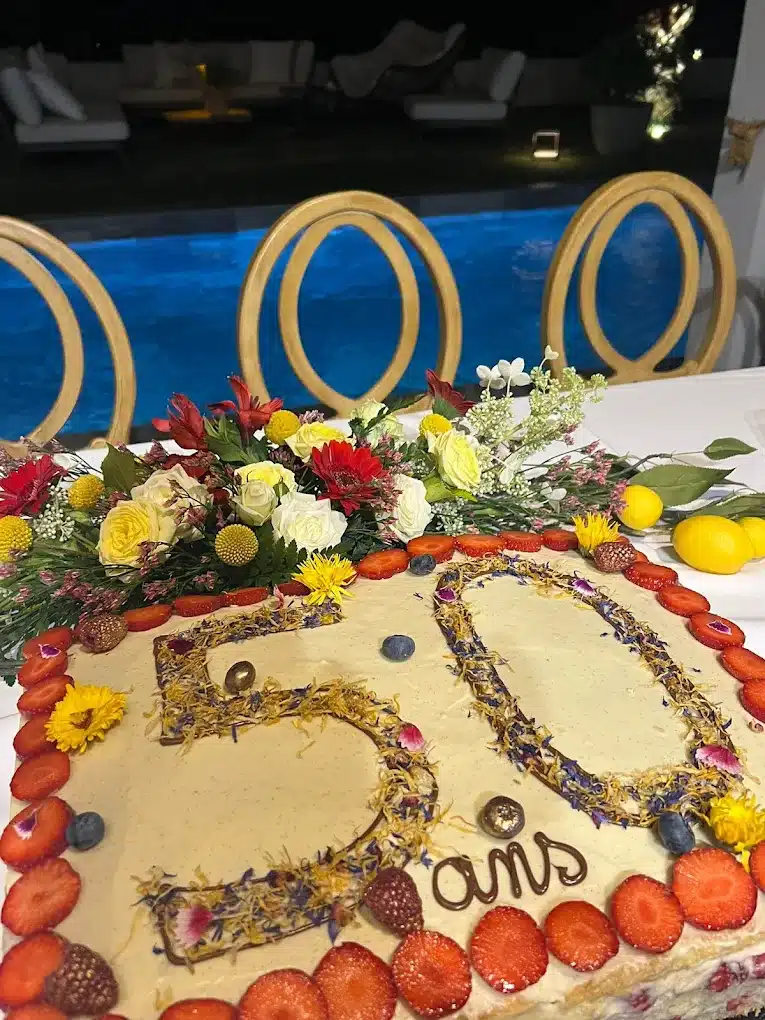 Gâteau d'anniversaire '50 ans' décoré de fleurs séchées, fraises et myrtilles, posé devant une piscine la nuit.