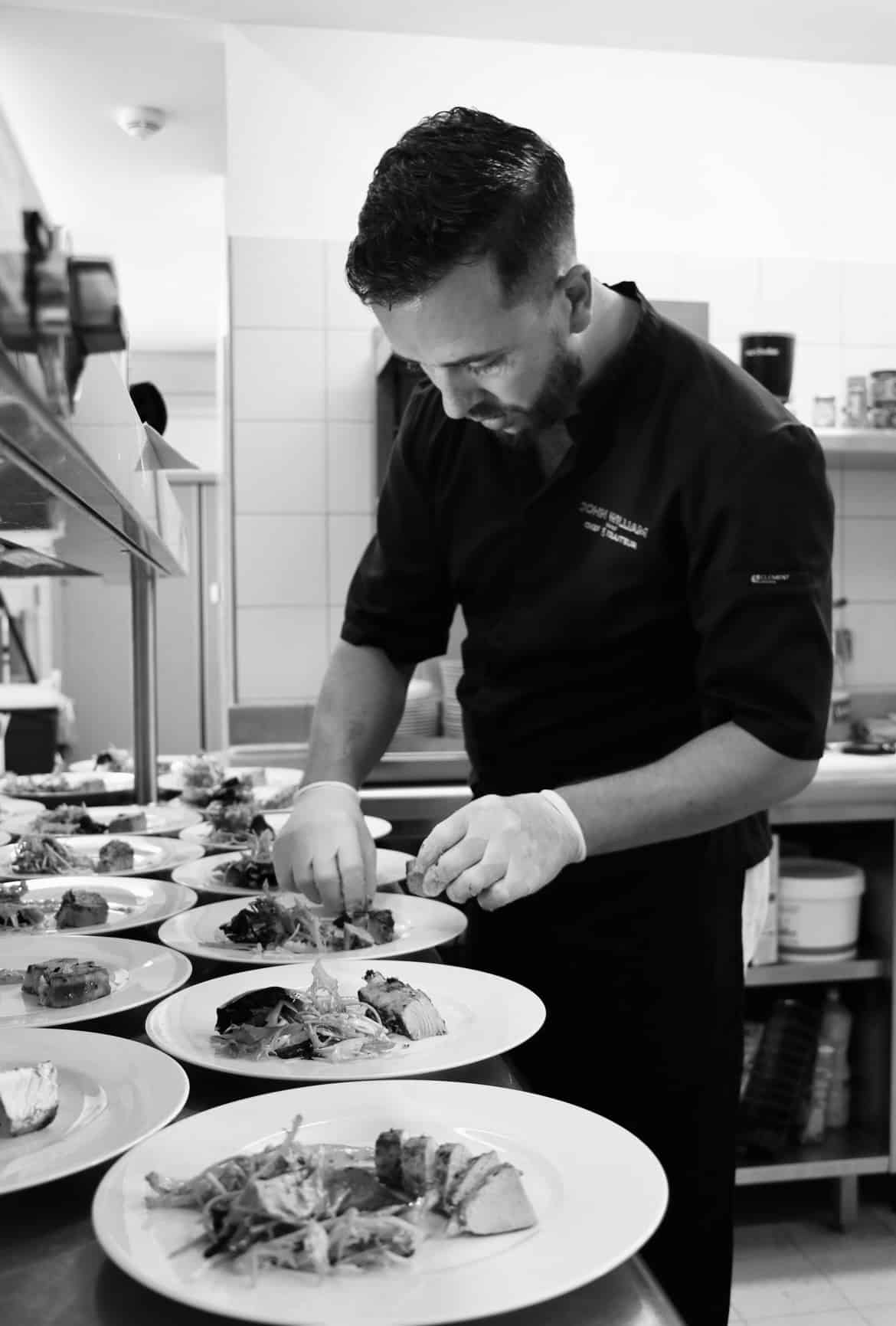 Le chef traiteur John William dresse avec soin des assiettes gastronomiques en cuisine.
