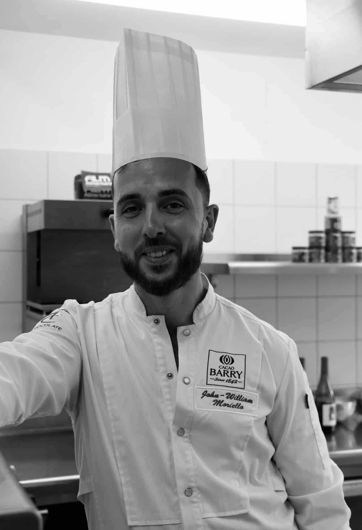Chef John-William Moriello souriant en veste Cacao Barry dans sa cuisine professionnelle.
