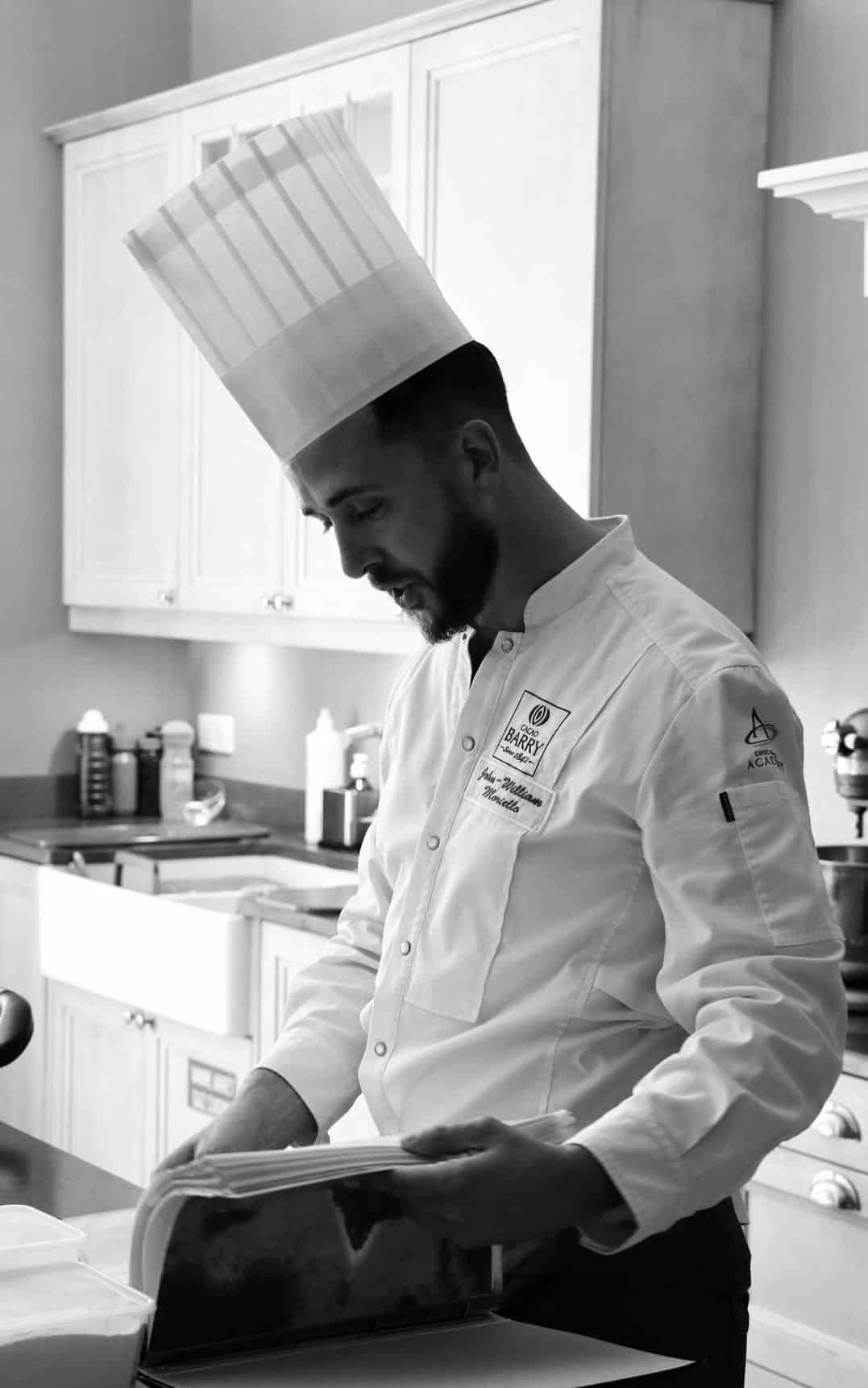 Chef John-William Moriello en toque et veste Cacao Barry lisant ses recettes.
