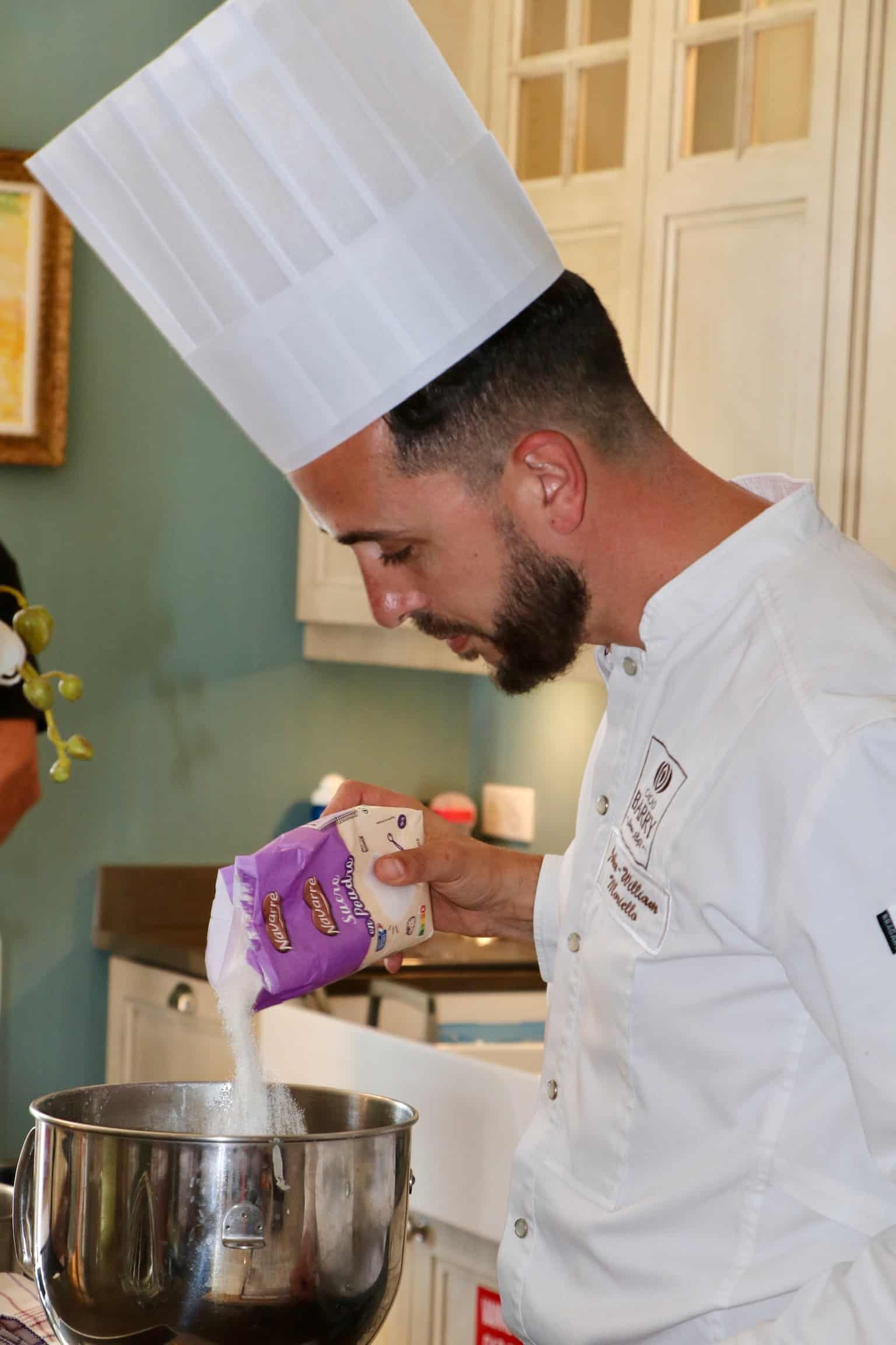Le chef Jean-William verse du sucre en poudre Navarre dans un bol mélangeur en inox.