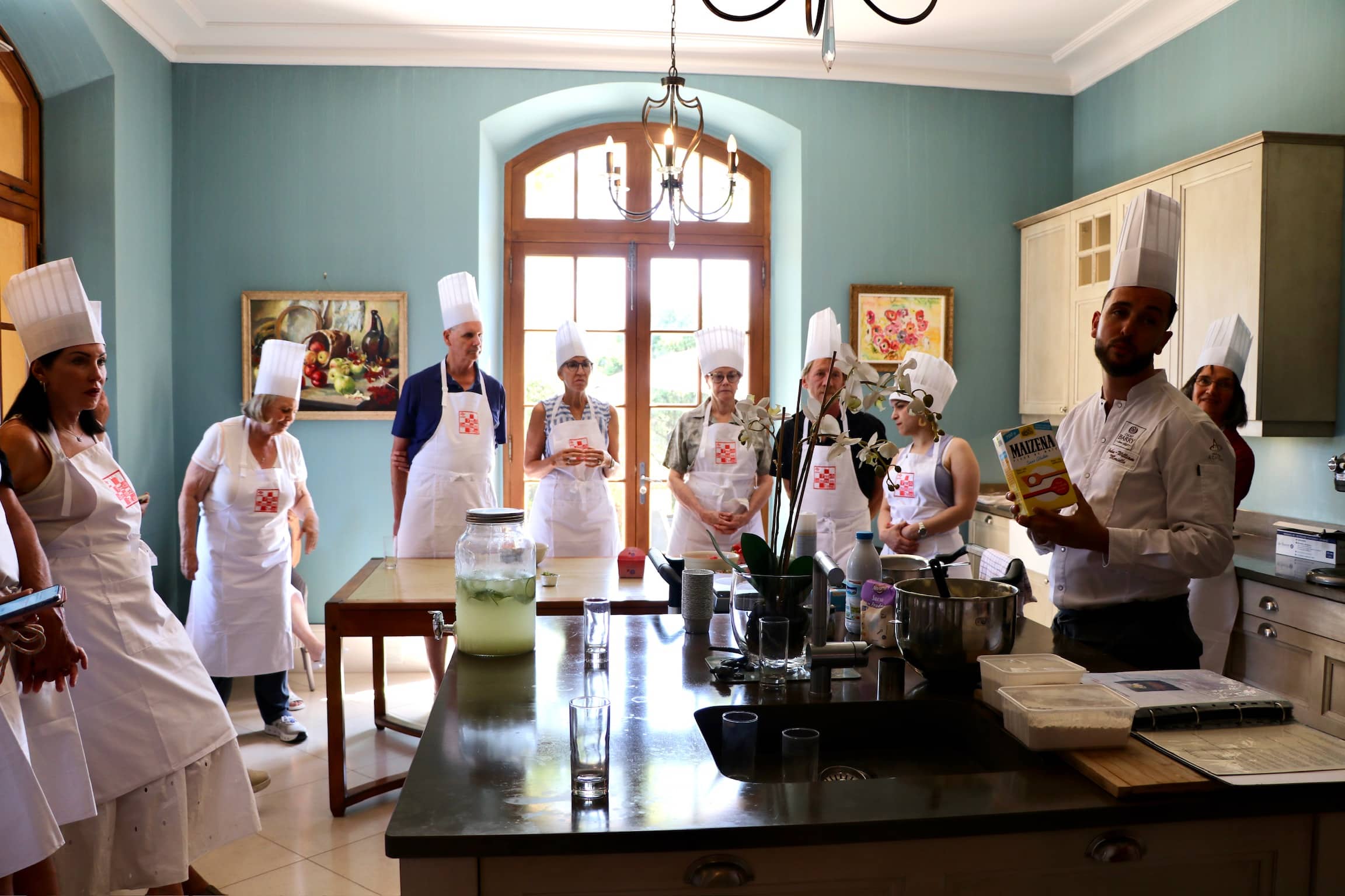 Chef présentant du Maizena à des élèves en tabliers lors d'un atelier culinaire.